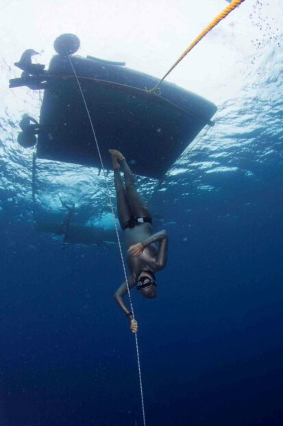 A freediver is descending underwater while holding a rope beside an anchored boat in deep blue water, 2K Mobile Wallpaper