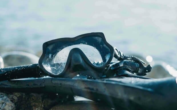 A close up of freediving gear resting on rocks near calm water, 2K Desktop Wallpaper