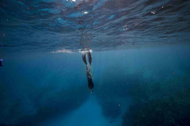 A person is freediving deep into clear blue ocean water with fins, HD Desktop Wallpaper