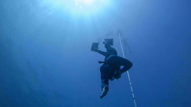 A freediver is descending into the deep blue ocean following a guide rope under clear sunlight, 4K Desktop Wallpaper