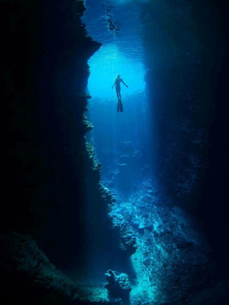 A freediver explores a deep blue underwater cave surrounded by rocky formations, HD Mobile Wallpaper