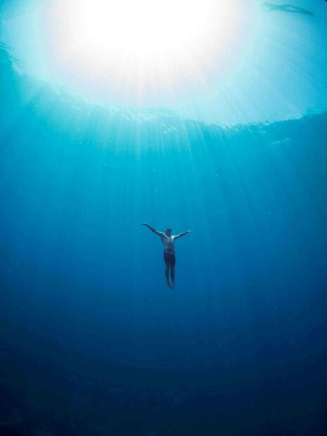 A freediver is swimming upwards through clear blue water with sunlight streaming down, HD Mobile Wallpaper