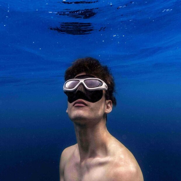 A freediver wearing a mask is submerged underwater surrounded by deep blue water, HD Mobile Wallpaper