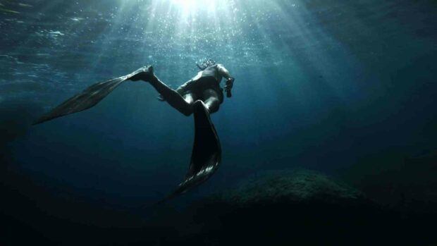 A freediver swims gracefully in deep ocean waters with sunlight filtering down, HD Desktop Wallpaper