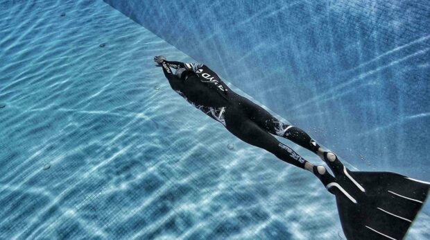 A freediver swims underwater with a monofin in a clear blue pool, HD Desktop Wallpaper