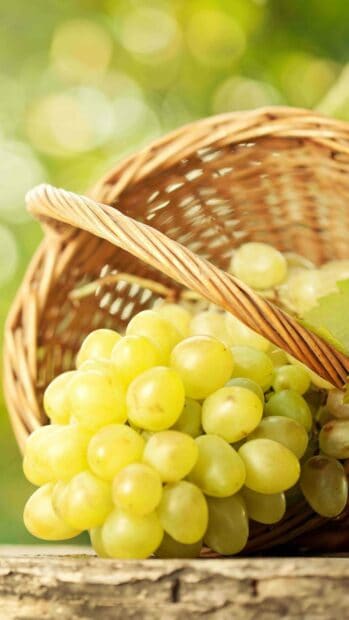 A close up of fresh green grapes spilling out of a wicker basket on a wooden surface, 4K Phone Wallpaper