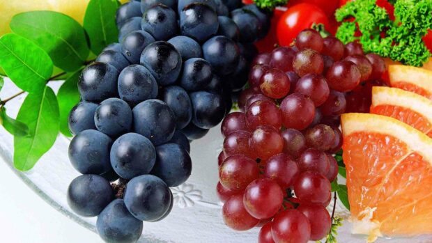 A close up of fresh ripe grapes alongside citrus slices and green leaves on a plate, HD Desktop Wallpaper