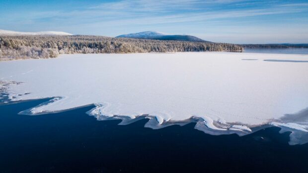 The frozen Arctic lake stretches beneath a clear blue sky with snowy shorelines and a forest in the distance, HD Desktop Wallpaper