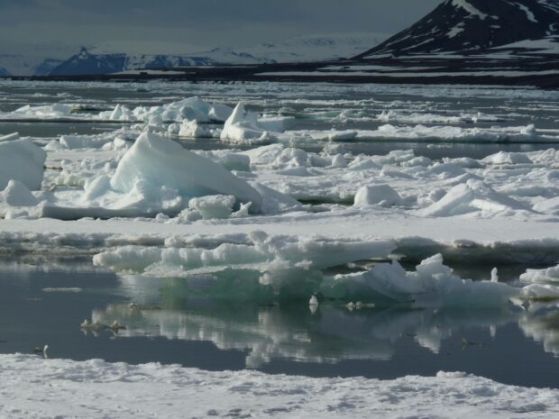 A cold Arctic landscape with ice floating on water and snow covered mountains in the background, 2K Desktop Wallpaper