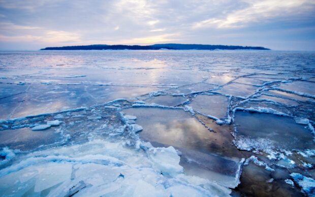 The frozen sea surface shows cracked ice sheets reflecting the cloudy sky in the arctic region, 2K Desktop Wallpaper