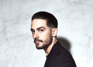 G Eazy stands confidently against a textured wall wearing a black suit, 4K Mobile Wallpaper