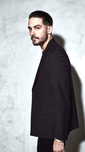G Eazy stands confidently against a textured wall wearing a black suit, 4K Mobile Wallpaper