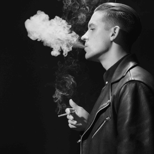 A man in a black leather jacket smoking while exhaling thick smoke with G Eazy Wallpapers, HD Mobile Wallpaper