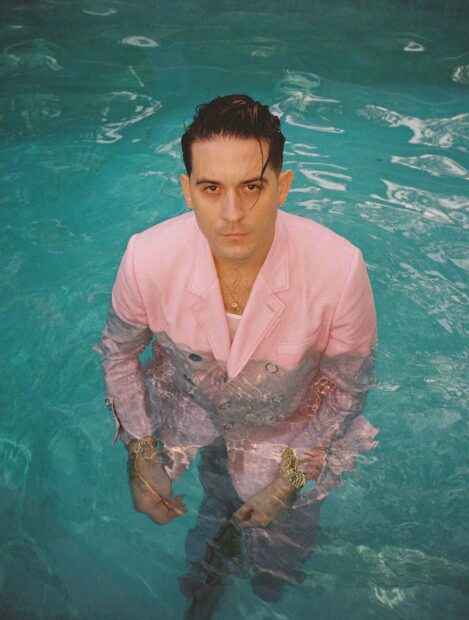 G Eazy is standing in a pool wearing a pink suit and looking directly at the camera, 2K Mobile Wallpaper