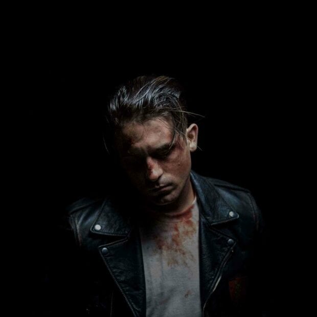 A moody G Eazy stands with a leather jacket and a blood stained shirt in a dark setting, HD Mobile Wallpaper