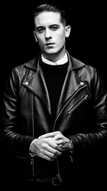 G Eazy is wearing a black leather jacket and posing with folded hands against a dark background, 4K Mobile Wallpaper