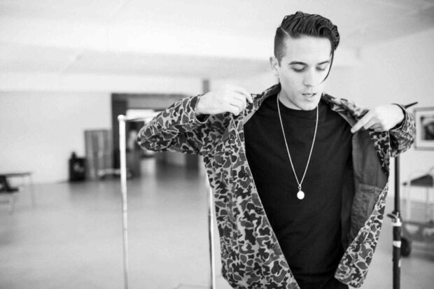 G Eazy is adjusting his jacket while looking down in a modern indoor setting, HD Desktop Wallpaper