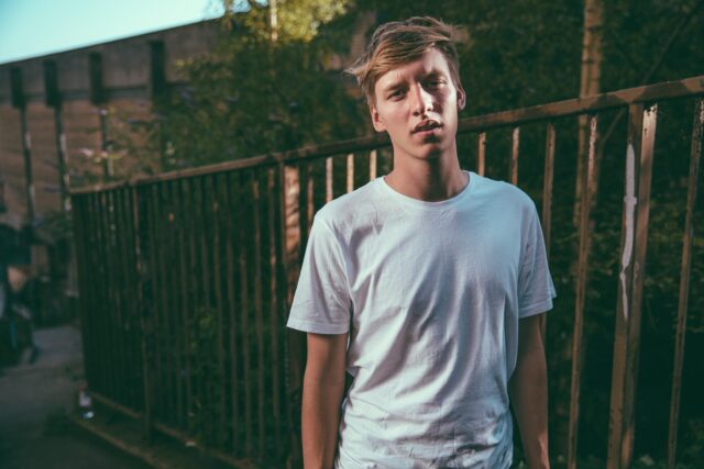 George Ezra Casual Pose in White T shirt Urban Background Wallpaper