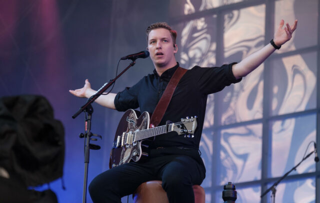George Ezra Live Performance Sitting with Guitar on Stage Wallpaper
