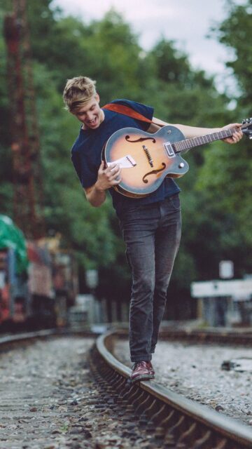 George Ezra Playing Guitar Walking on Train Tracks Nature Background Wallpapers