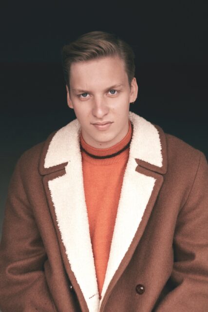 George Ezra close up portrait in brown shearling coat and orange sweater wallpaper