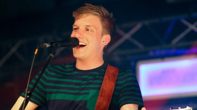 George Ezra live performance smiling with guitar on stage wallpaper
