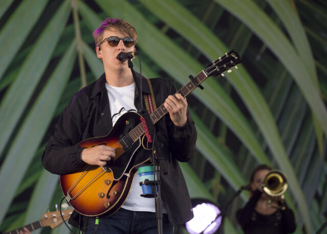 George Ezra performing live on stage playing guitar with tropical background for wallpapers