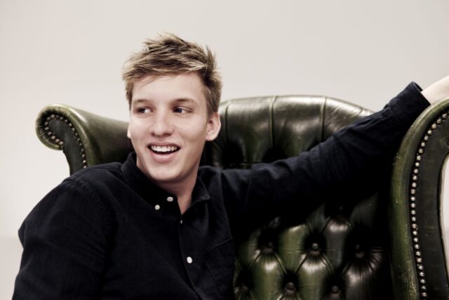 George Ezra relaxed on vintage leather chair casual smile wallpaper