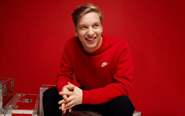 George Ezra smiling in red Nike sweatshirt vibrant wallpaper background