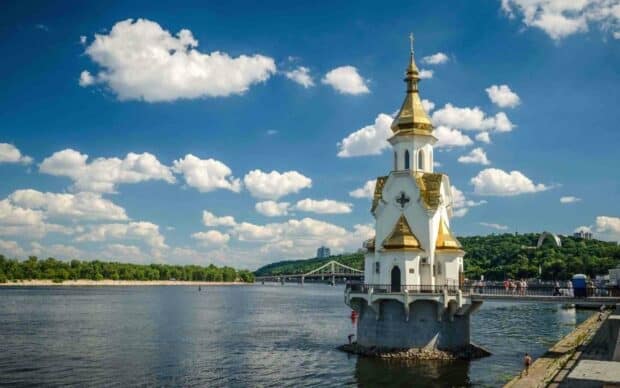 A golden church tower stands above the river in Ukraine with a blue sky and clouds, HD Desktop Wallpaper