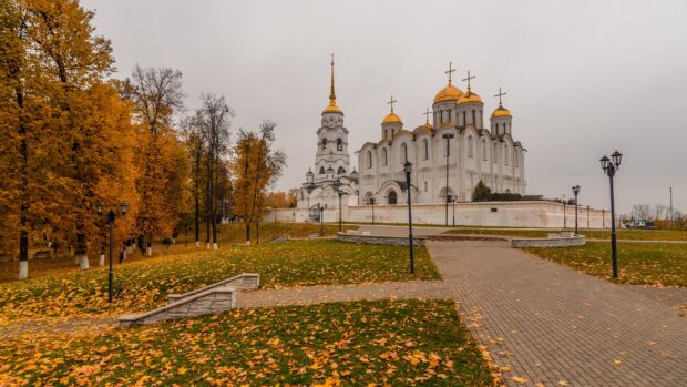 A historic cathedral with golden domes surrounded by autumn trees and fallen leaves, 4K Desktop Wallpaper