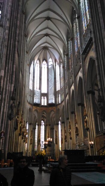 The cathedral interior shows tall arches and stained glass with people inside, 2K Mobile Wallpaper