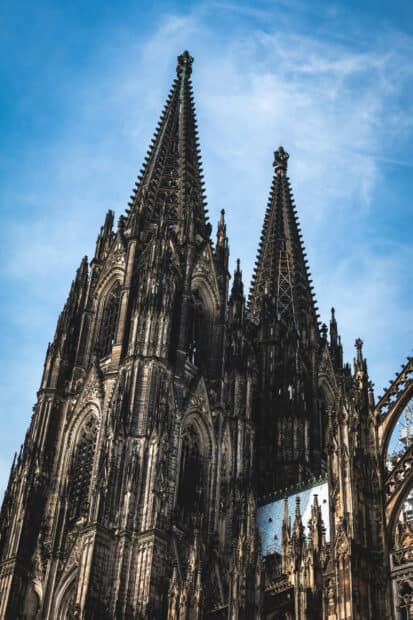 The cathedral spires display intricate gothic architecture under a blue sky with clouds, 2K Mobile Wallpaper