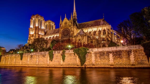 The cathedral illuminated at night reflects in the river under a deep blue sky featuring cathedral wallpapers, 4K Desktop Wallpaper