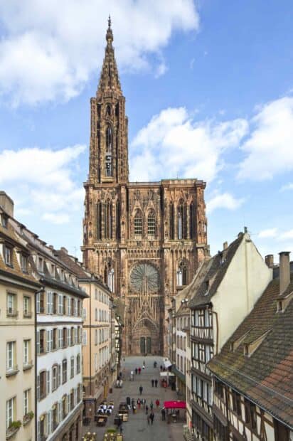 A Gothic cathedral stands tall surrounded by old buildings and people walking, 2K Mobile Wallpaper