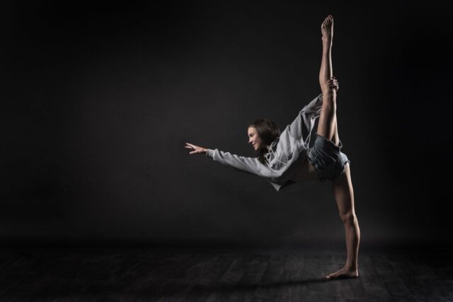 Graceful Contemporary Dance Pose Woman Stretching in Dark Studio Wallpaper