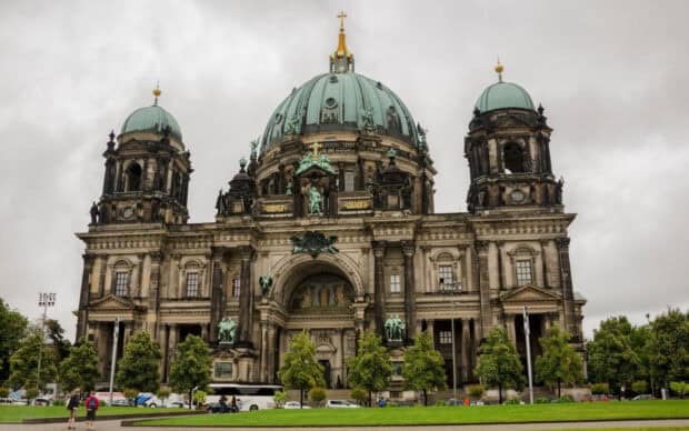 A grand historic cathedral with green domes and intricate sculptures stands under a cloudy sky, HD Desktop Wallpaper