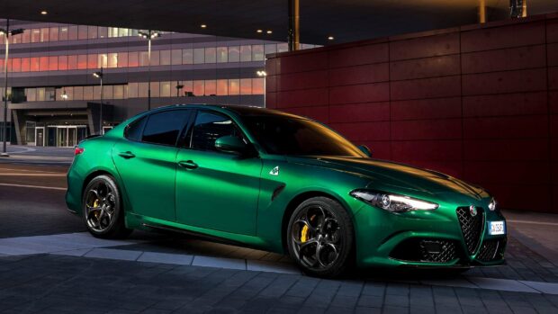 A green Alfa Romeo car is parked on a modern city street at dusk with building lights reflecting on its surface, 2K Desktop Wallpaper