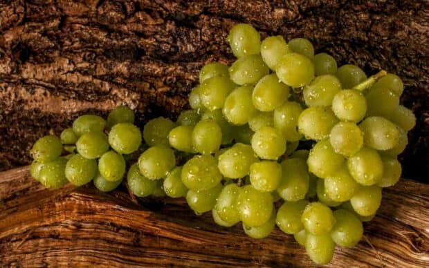 A bunch of green grapes with water droplets lying on a textured wooden surface, HD Desktop Wallpaper