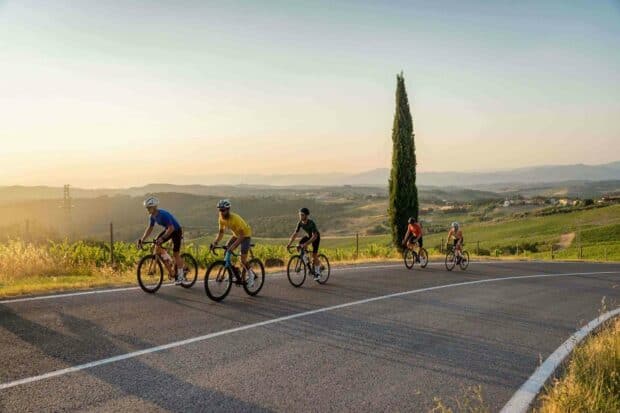 A group of cyclists enjoy a ride on a winding road surrounded by hills and greenery in a peaceful evening, HD Desktop Wallpaper