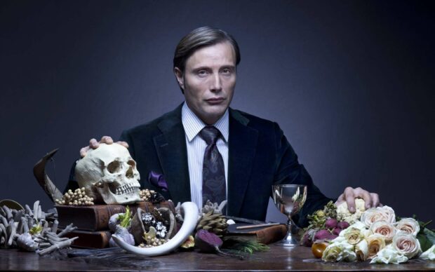 Hannibal Mads Mikkelsen sits behind a table with a skull and flowers, 2K Desktop Wallpaper