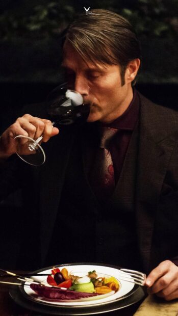 Hannibal is shown drinking red wine while seated at a table with gourmet food, HD Phone Wallpaper