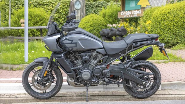 A grey Harley Davidson Pan America 1250 adventure motorcycle parked on the street with green bushes in the background, 4K Desktop Wallpaper