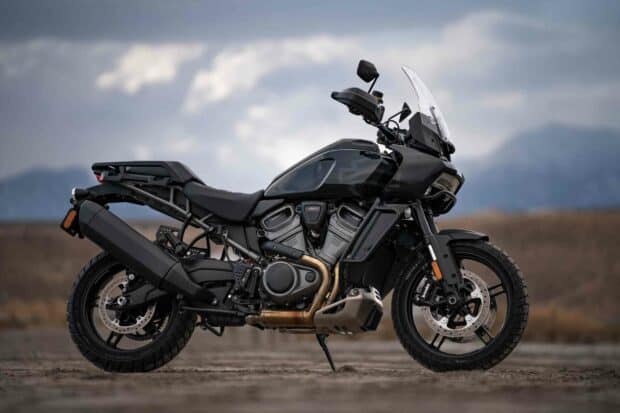 A black Harley Davidson Pan America 1250 motorcycle parked outdoors with mountains and cloudy sky in the background, 2K Desktop Wallpaper