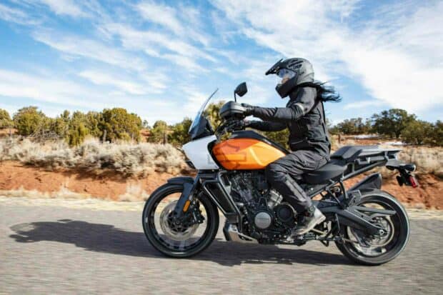 A rider wearing full gear rides a Harley Davidson Pan America 1250 on an open road under a blue sky, HD Desktop Wallpaper