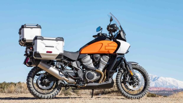 A Harley Davidson Pan America 1250 motorcycle parked outdoors on a dirt road with mountains in the background