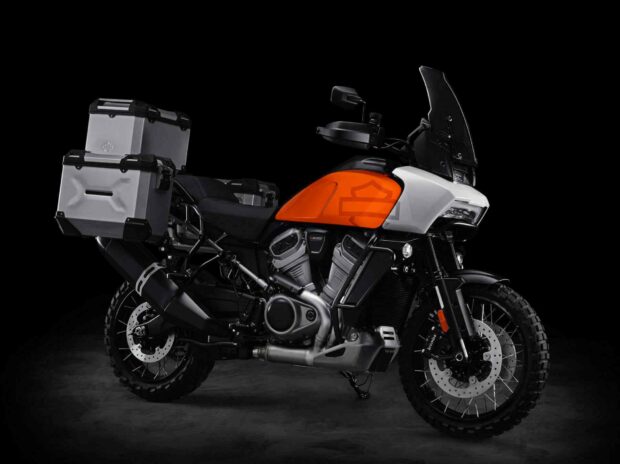 The Harley Davidson Pan America 1250 is a powerful adventure motorcycle with an orange fuel tank and silver panniers