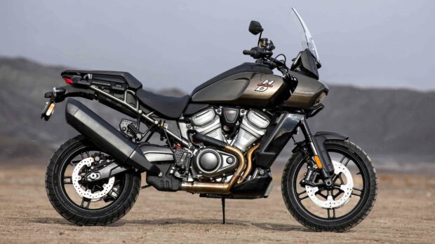A Harley Davidson Pan America 1250 motorcycle parked on a sandy surface with a mountainous background, 4K Desktop Wallpaper