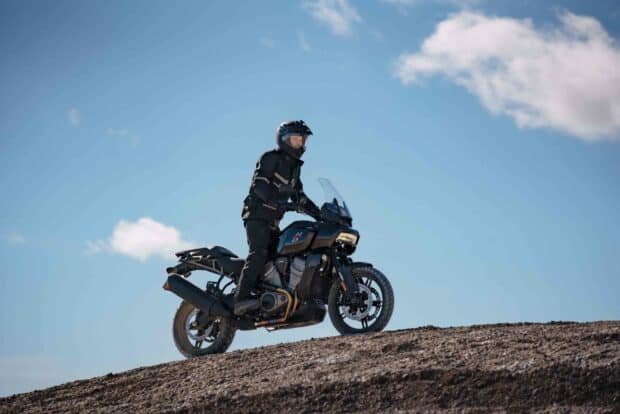 A rider on a Harley Davidson Pan America 1250 motorcycle traveling on a dirt hill under a clear blue sky, 2K Desktop Wallp