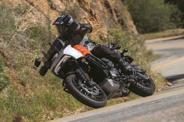 A rider on a Harley Davidson Pan America 1250 is leaning into a sharp turn on a winding road, HD Desktop Wallpaper